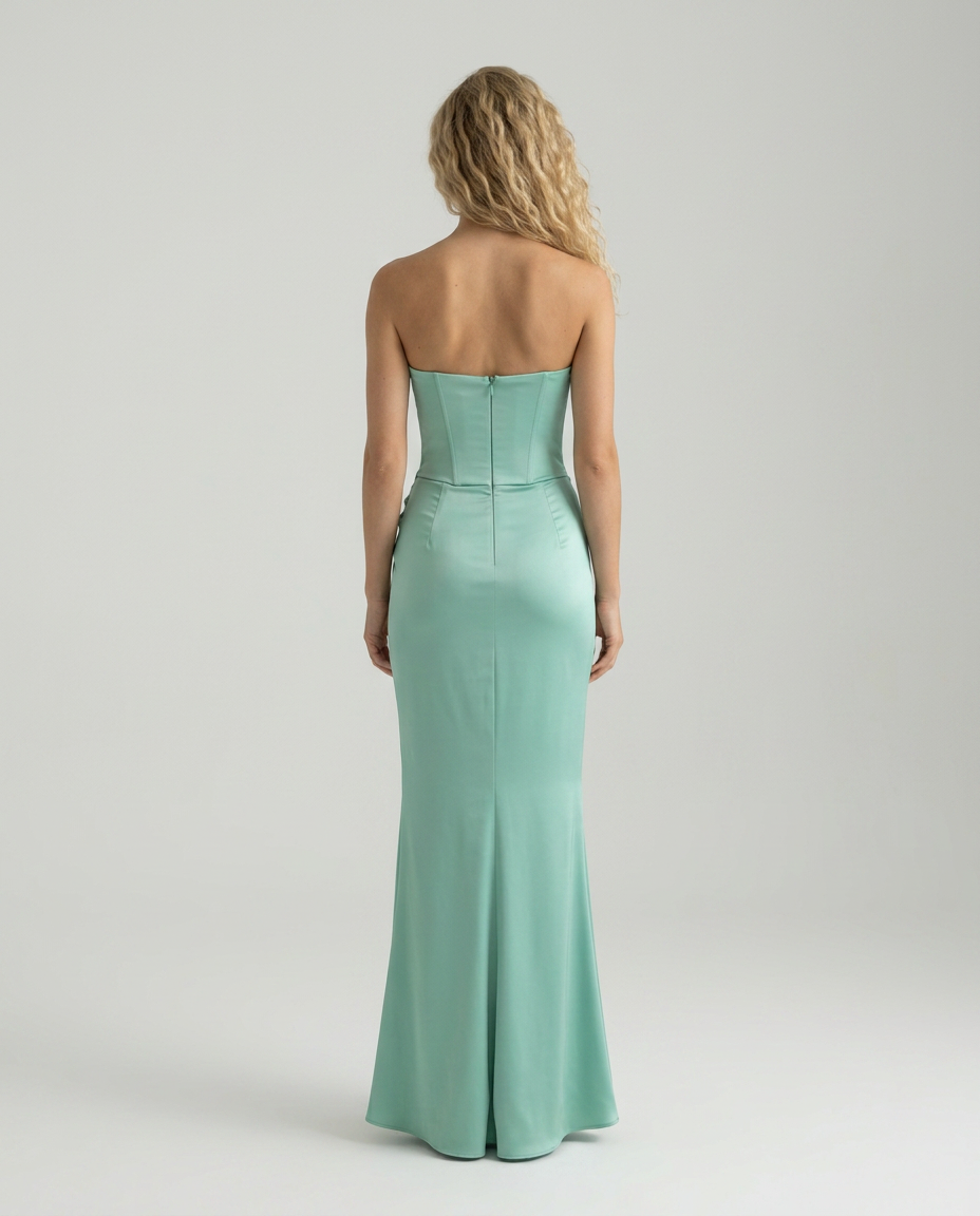 Woman modeling a long strapless dress with elegant draping and a fitted silhouette on a plain background.