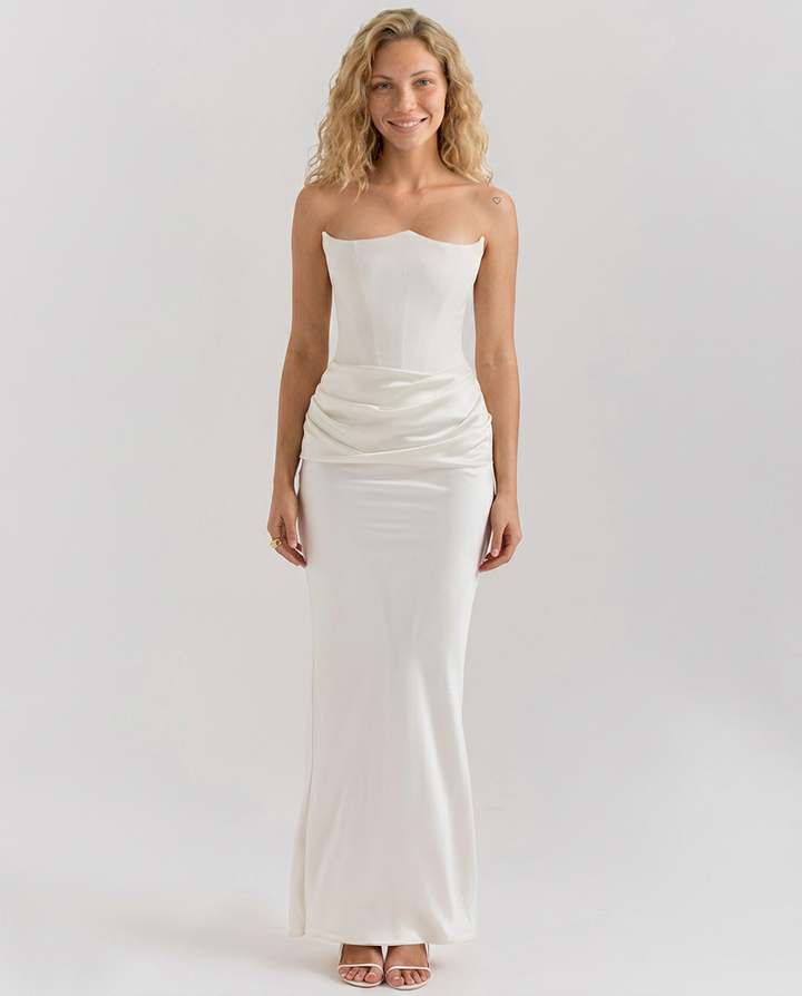 Woman wearing a long event dress with subtle waist gathering and sleek lines on a plain background.