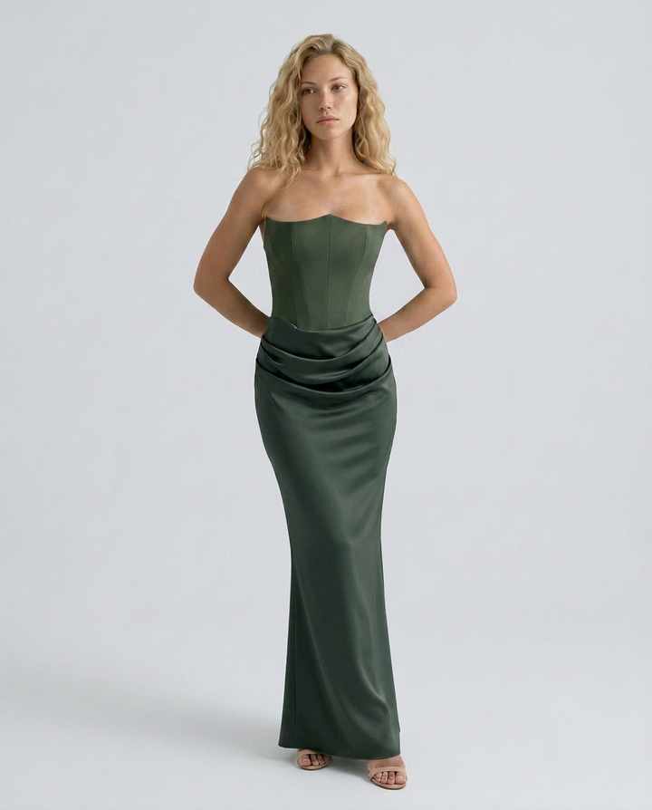 Woman in a formal maxi dress with elegant drape detailing and smooth finish on a plain background.