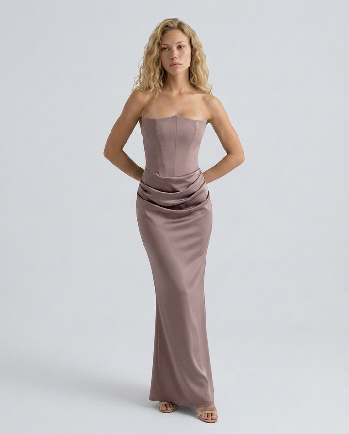 Woman showcasing a formal maxi dress with a refined silhouette and draped waistline on a plain background.