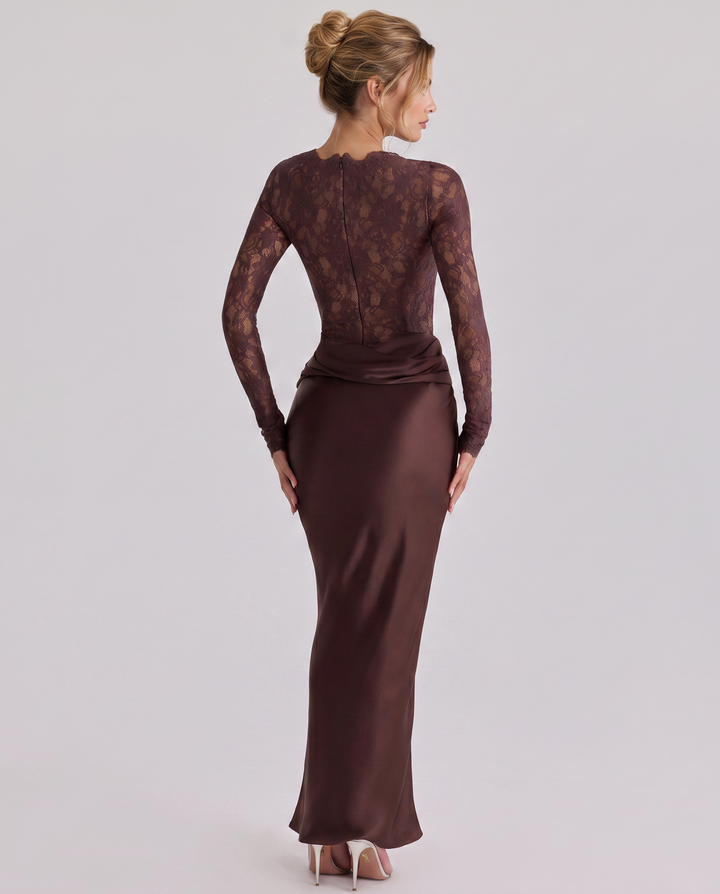 Woman posing in a high neckline lace bodice dress with a draped maxi skirt against a plain background.