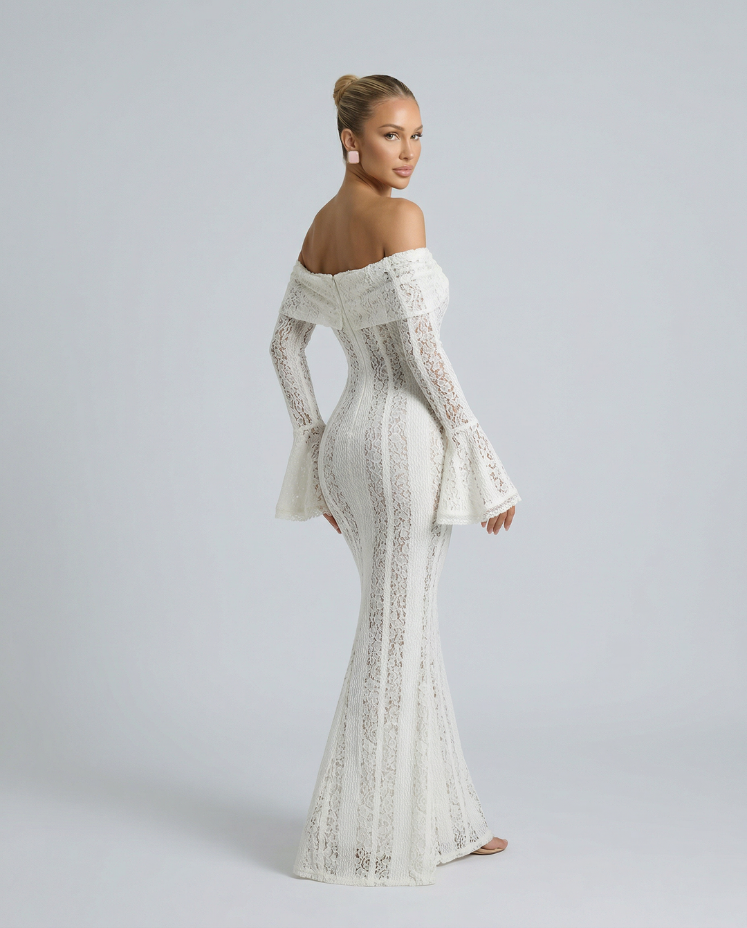 Woman in an off-shoulder floral lace dress with long sleeves on a plain background.
