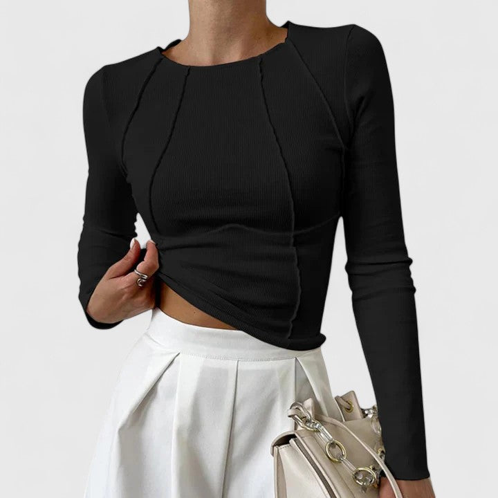 Female model in a chic fitted top standing against a plain background.