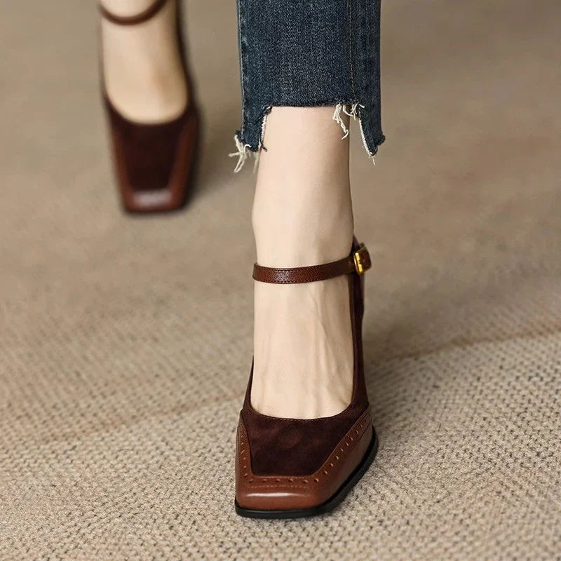Woman styling square toe ankle strap heels with tailored trousers on a plain background.