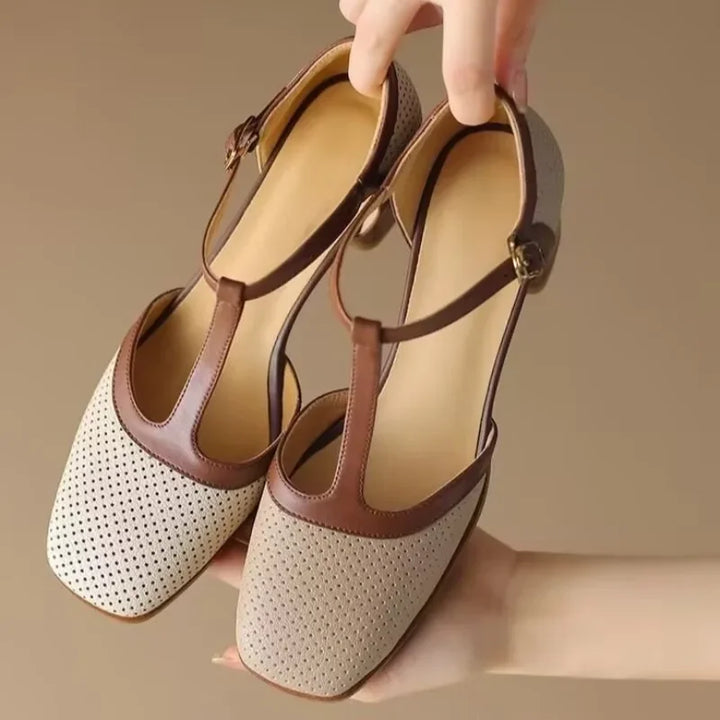 Woman styling cream perforated block heel shoes with a tan strap on a plain background.