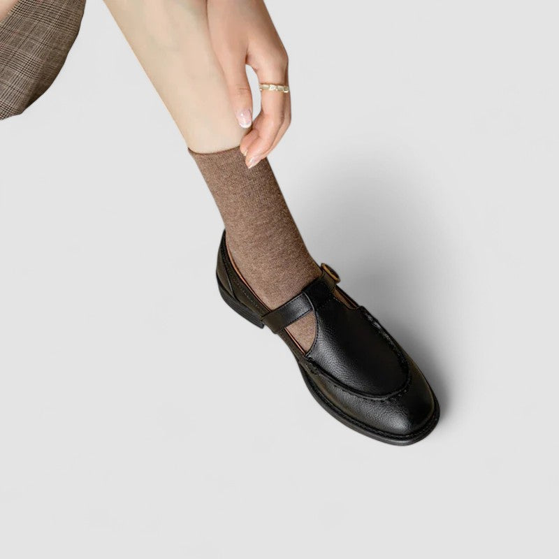 Woman modelling black square toe shoes with a simple strap on a plain background.