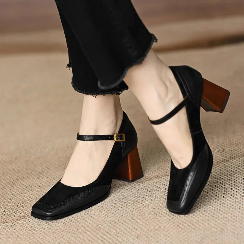 Female posing in polished block heel pumps with decorative stitching on a plain background.
