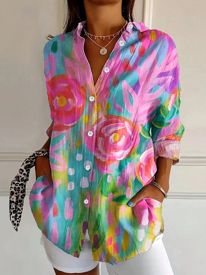 Female model wearing a colorful floral button-front blouse on a plain background.