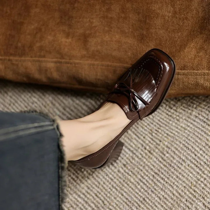 Woman standing in classic tassel loafer pumps with rounded toes on a plain background.