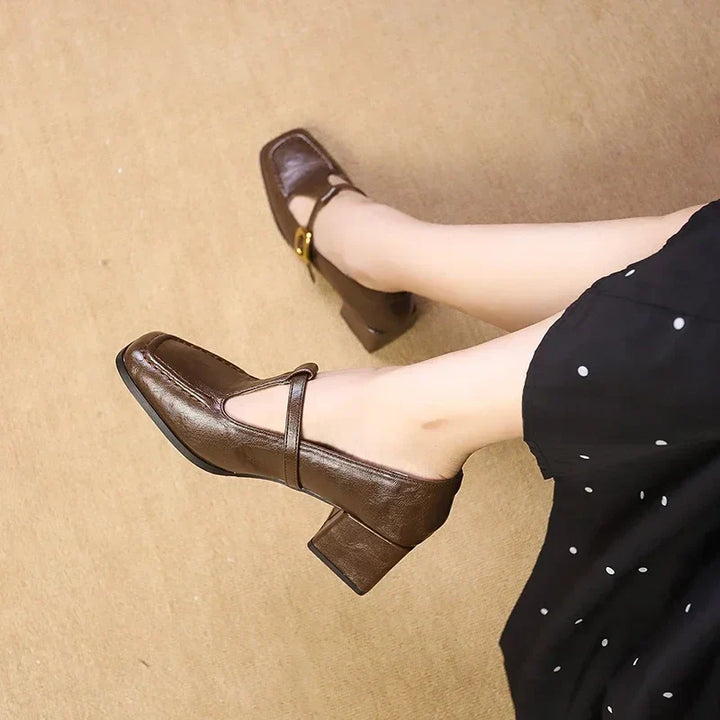 Woman styling buckle strap square toe heels on a plain background.
