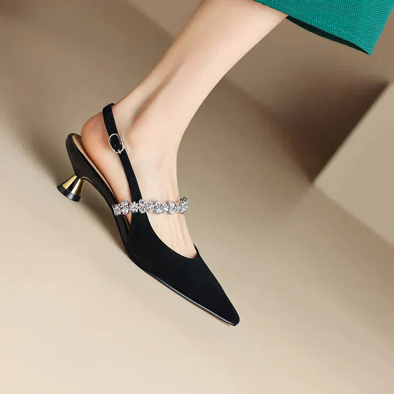 Female wearing metallic pointed toe heels with delicate crystal embellishment on a plain background.