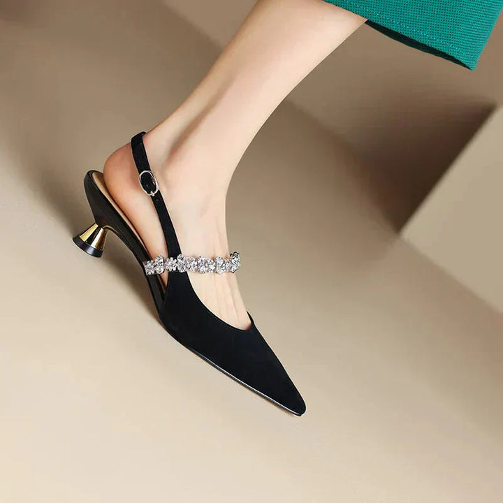 Female wearing metallic pointed toe heels with delicate crystal embellishment on a plain background.
