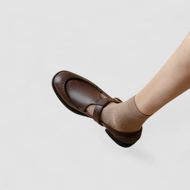 Female wearing classic Mary Jane style shoes on a plain background.
