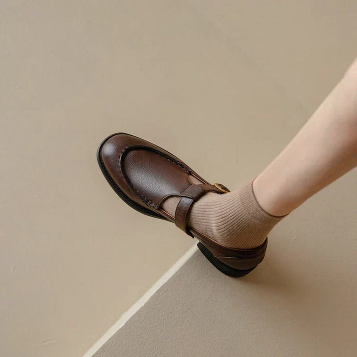 Woman showcasing retro style shoes with stitched detail on a plain background.