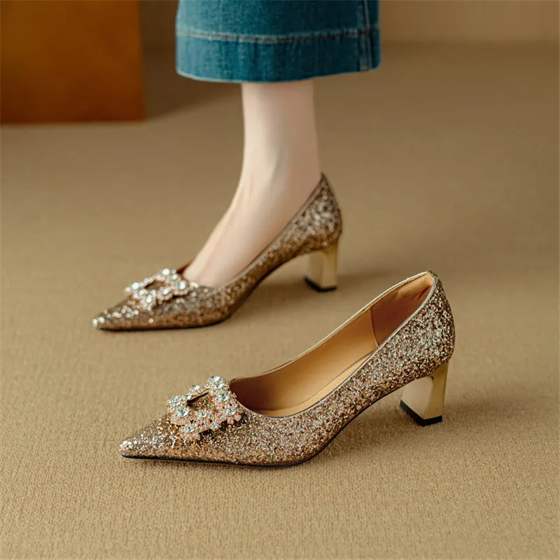Female model showcasing shimmering dress heels with buckle detail on a plain background.