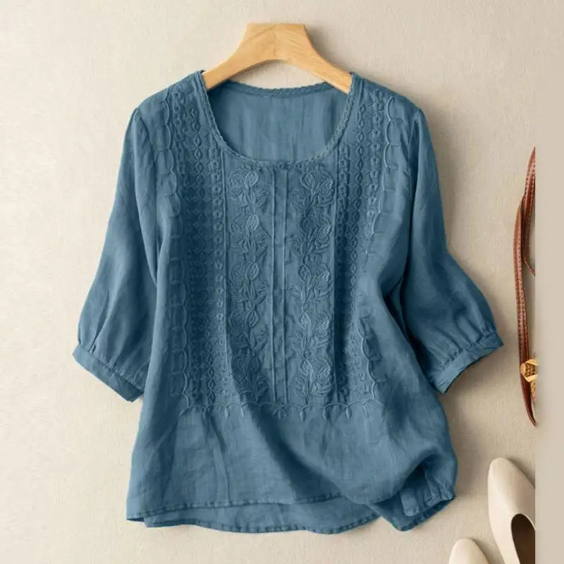 Relaxed embroidered blouse with a clean round neckline on a plain background.
