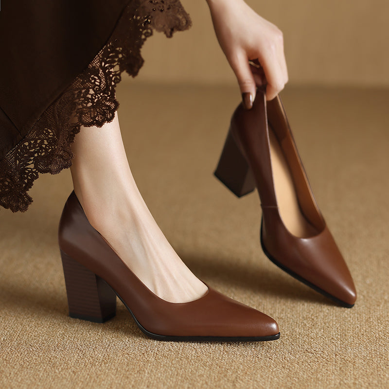 Woman wearing tan pointed toe block heel pumps on a plain background.