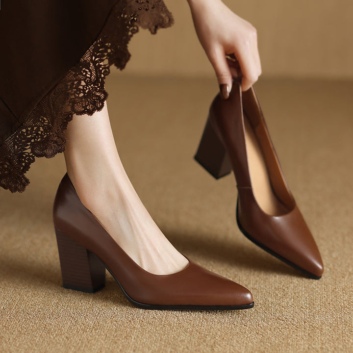 Woman wearing tan pointed toe block heel pumps on a plain background.