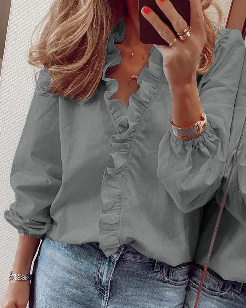 Female modelling a relaxed blouse with decorative ruffle trim and long sleeves.