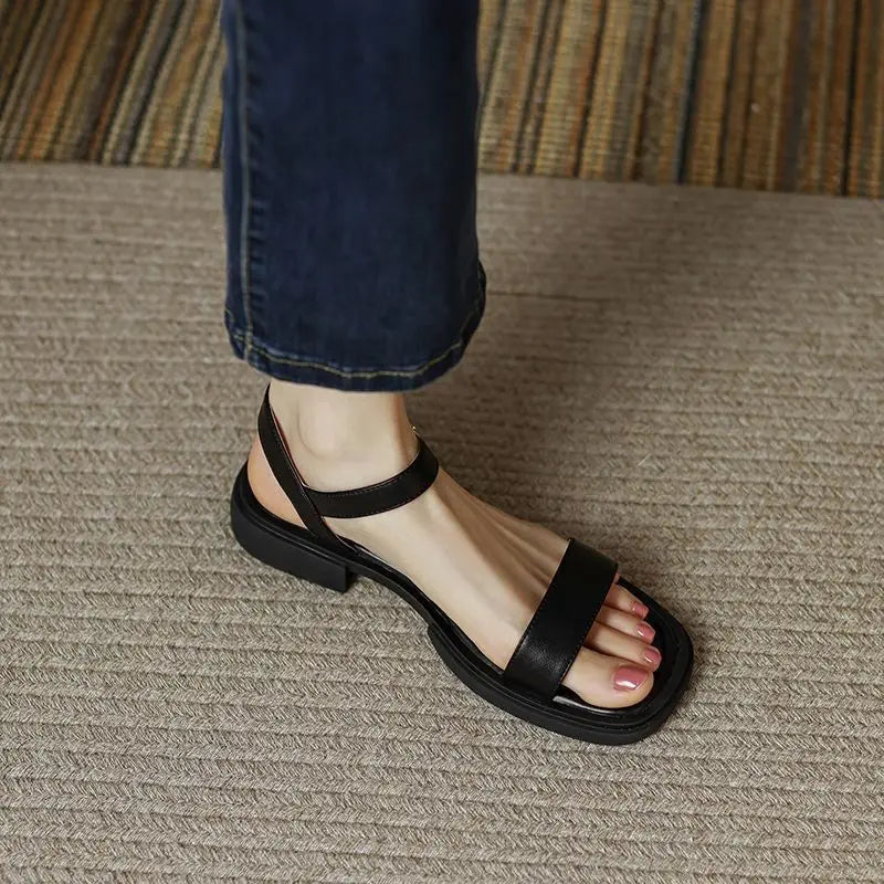 Woman showing low heel sandals with ankle strap on a plain background