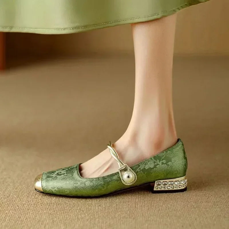 Woman styling square toe Mary Jane heels with pearl strap detail on a plain background.