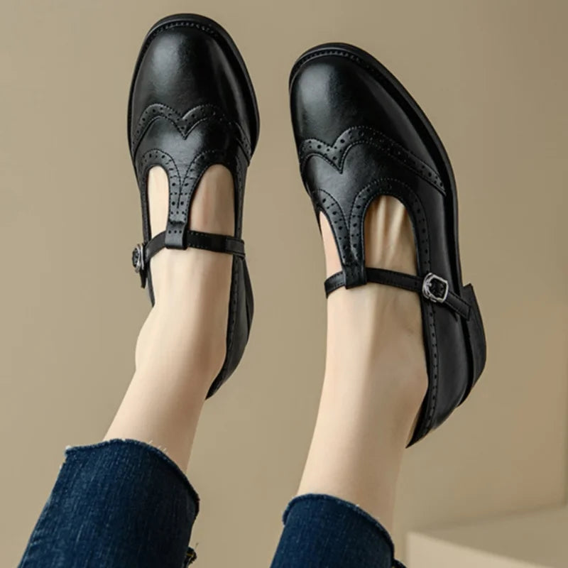 Woman styling brogue detail Mary Jane shoes on a plain background.