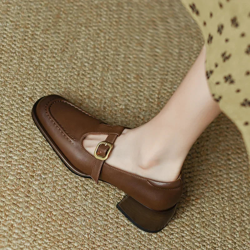 Female model wearing T-bar strap shoes with a square toe on a plain background.