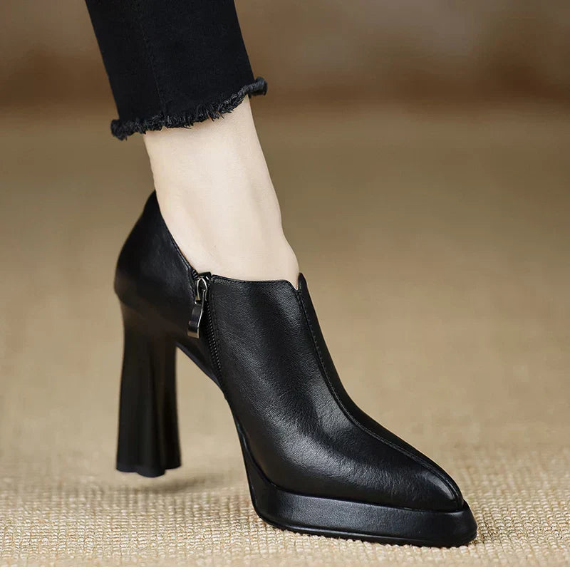 Woman showcasing side zip ankle high heel pumps on a plain background.