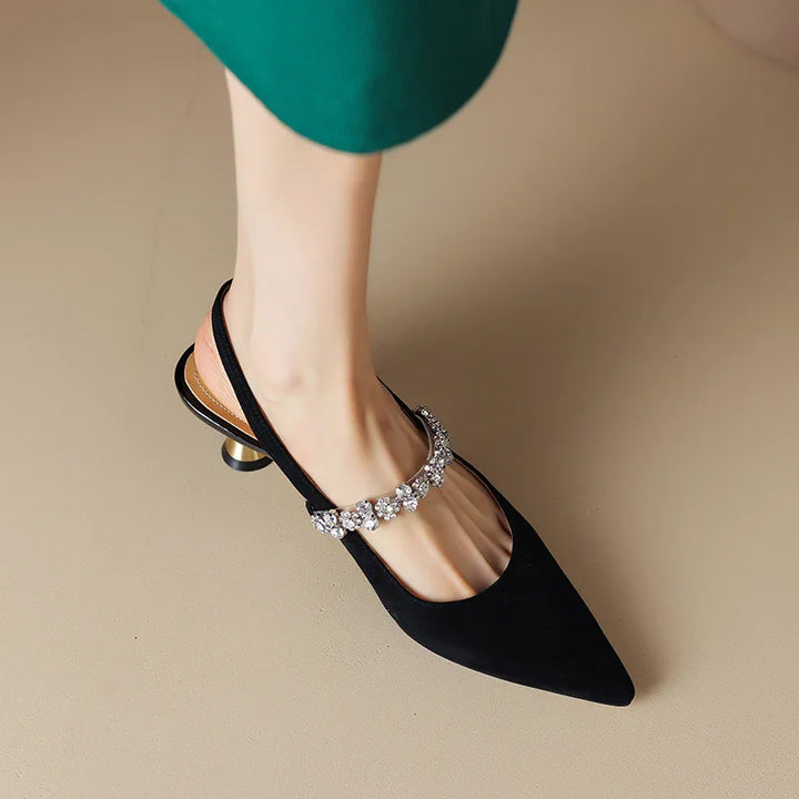Female standing in sleek pointed heels with embellished strap detail on a plain background.