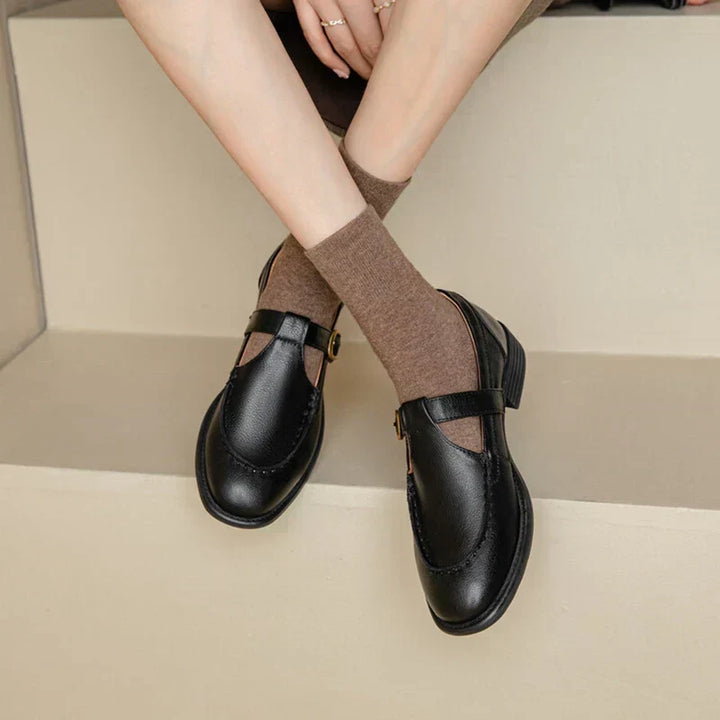 Woman wearing retro Mary Jane shoes with a buckle strap on a plain background.