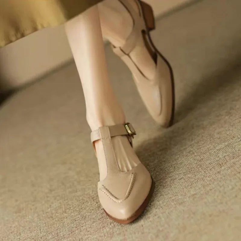 Woman showcasing cream low heel buckle shoes on a plain background.