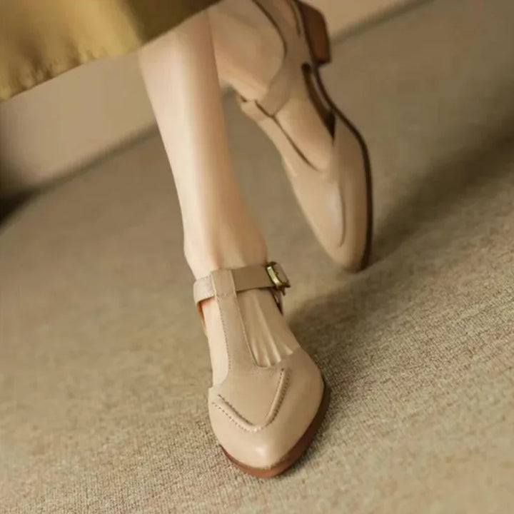 Woman showcasing cream low heel buckle shoes on a plain background.