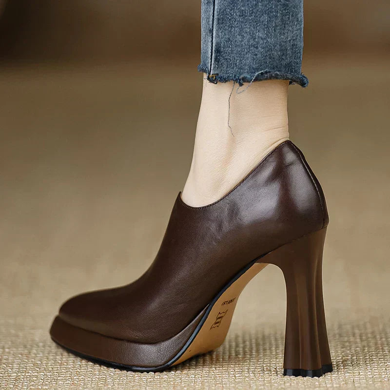 Woman styling ankle high heeled pumps with a sleek finish on a plain background.