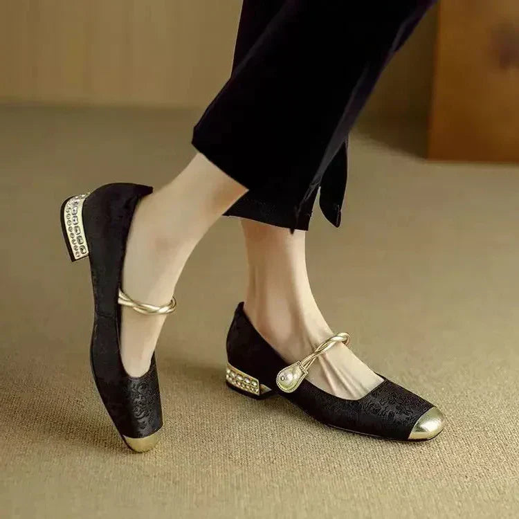 Female modelling low block heel Mary Jane shoes with shimmer detail on a plain background.