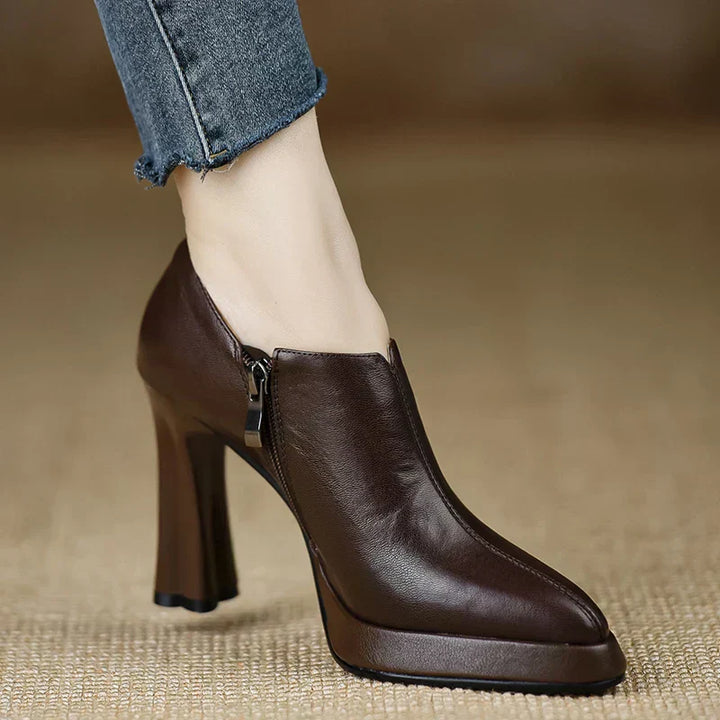 Woman wearing black ankle high platform heel pumps on a plain background.