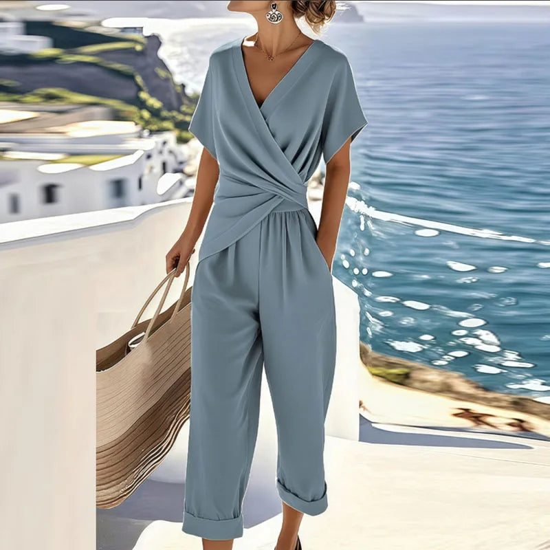 Woman in a lightweight wrap-front top and relaxed trousers on a plain background.