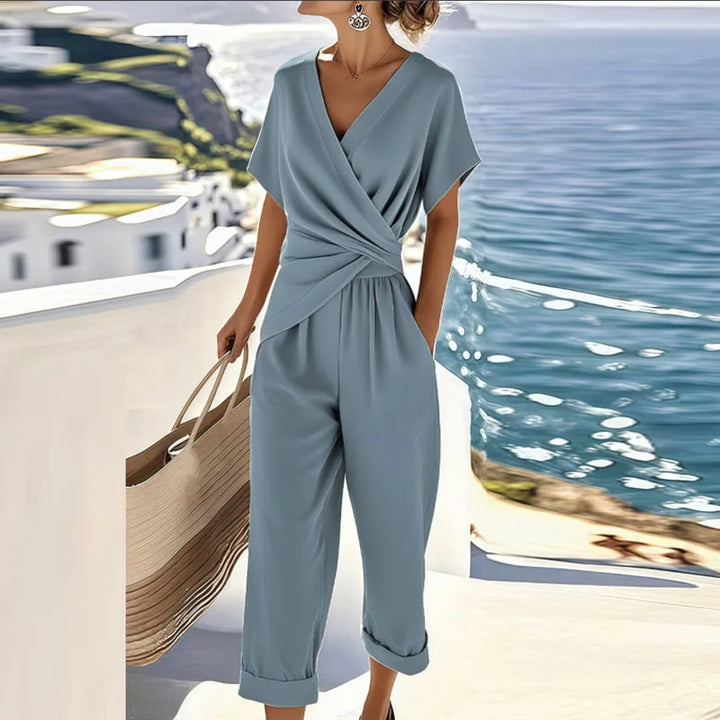 Woman in a lightweight wrap-front top and relaxed trousers on a plain background.