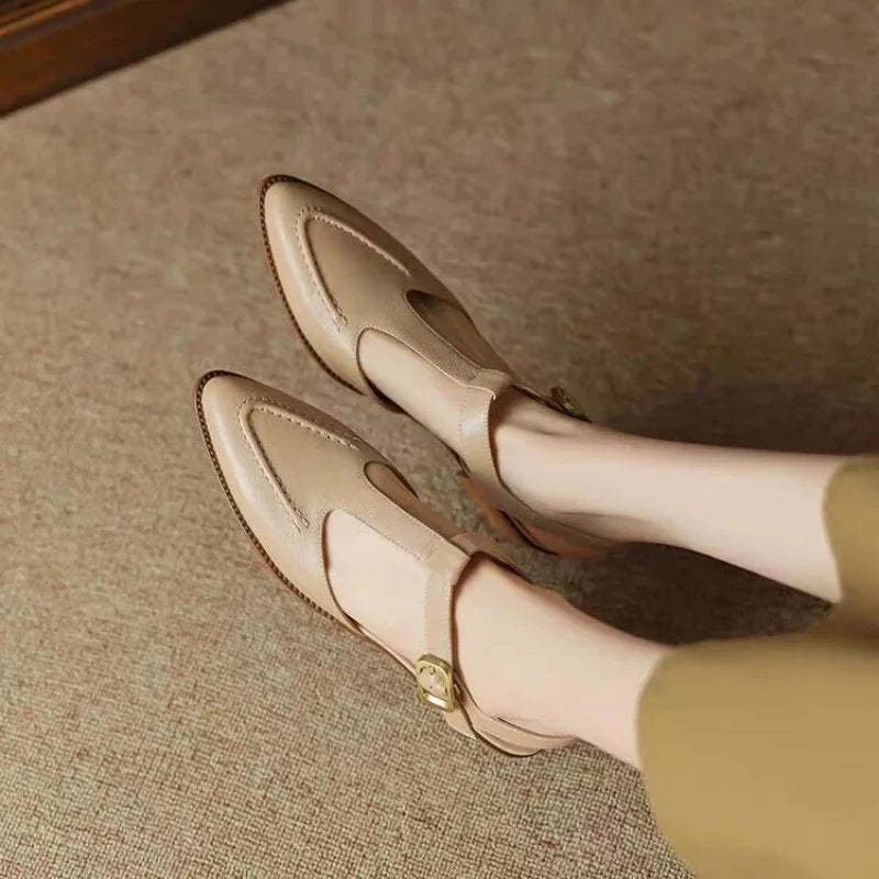 Woman styling structured buckle shoes with simple trousers on a plain background.