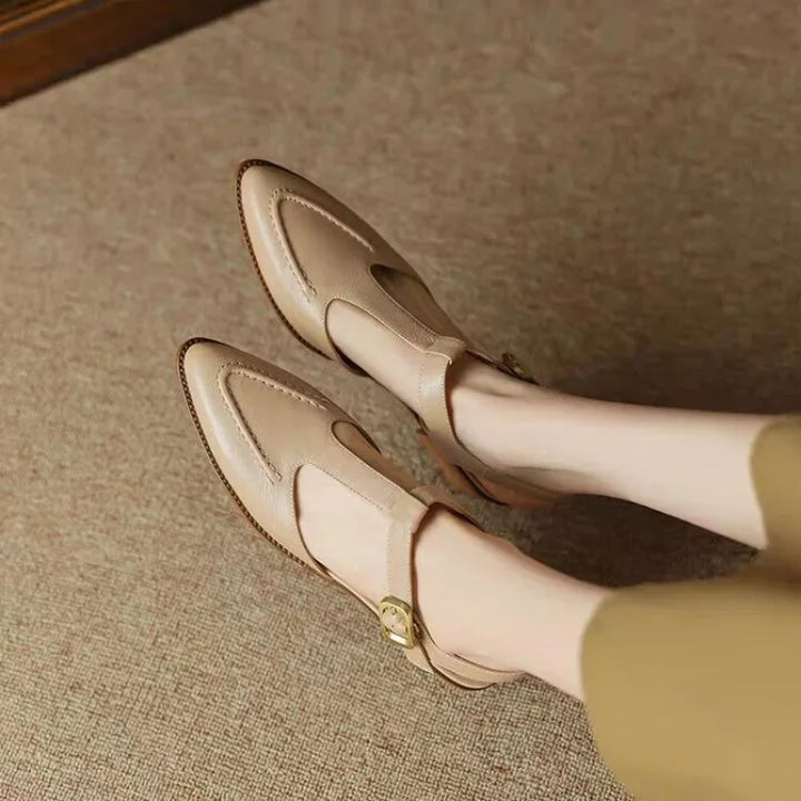 Woman styling structured buckle shoes with simple trousers on a plain background.