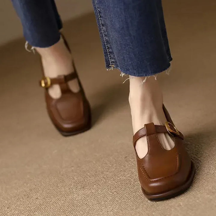 Female model wearing structured square toe shoes against a plain background.