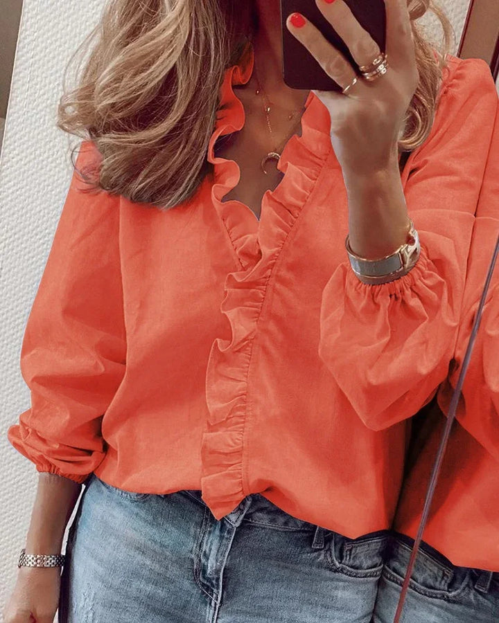 Woman wearing a ruffle neckline blouse with gathered balloon sleeves against a plain background.