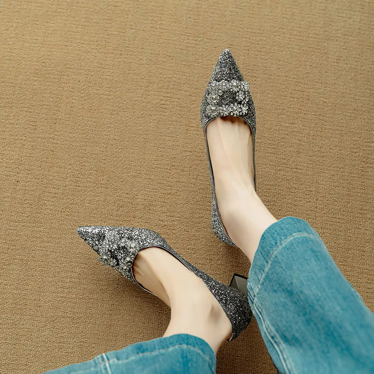 Woman standing in glitter occasion heels with a polished buckle detail on a plain background.