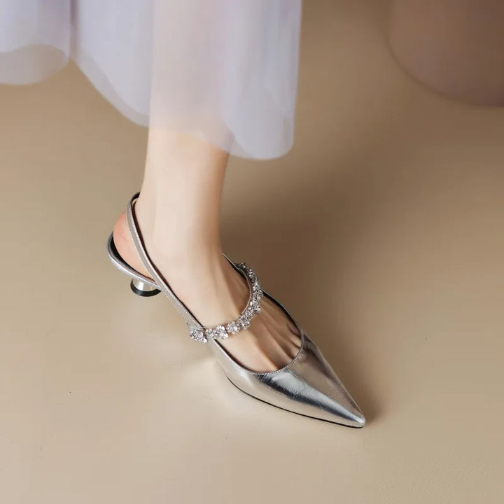 Woman posing in glossy slingback heels with sparkling instep detail on a plain background.