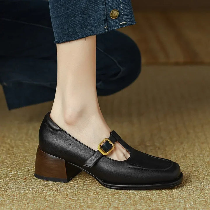 Female model showing low heel T-bar shoes on a plain background.