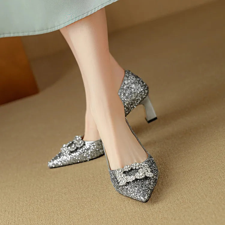 Woman wearing dressy glitter heels with rhinestone buckle accent on a plain background.