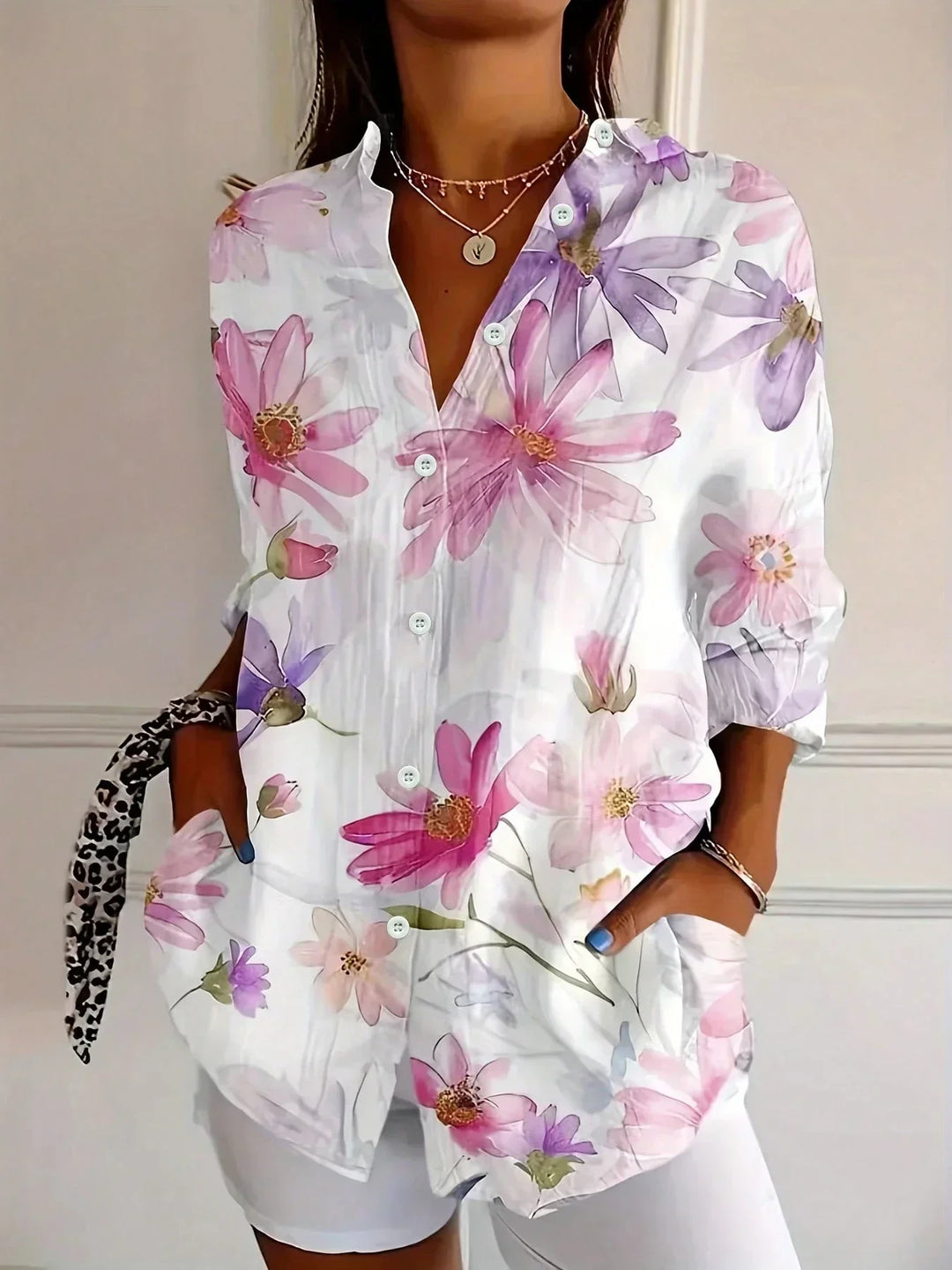 Woman wearing a colorful printed blouse in a simple studio setting.