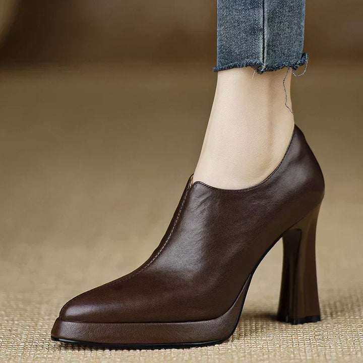 Female model wearing flared heel platform pumps in black on a plain background.