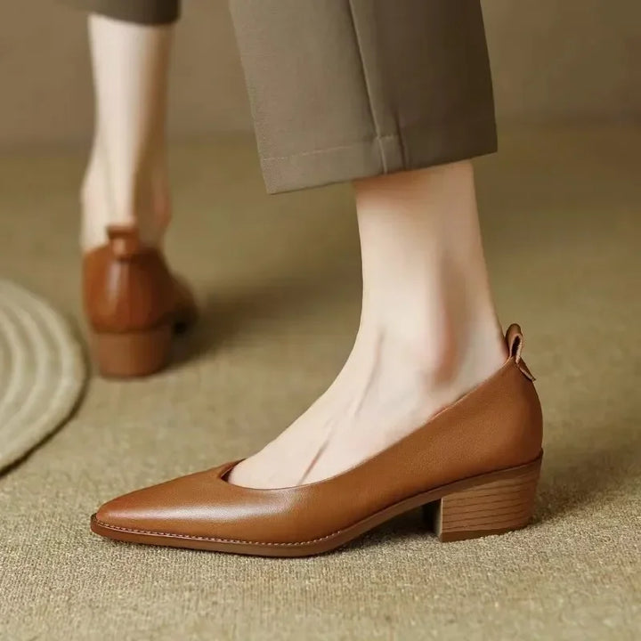 Female styling block heel shoes with a clean outfit on a plain background.
