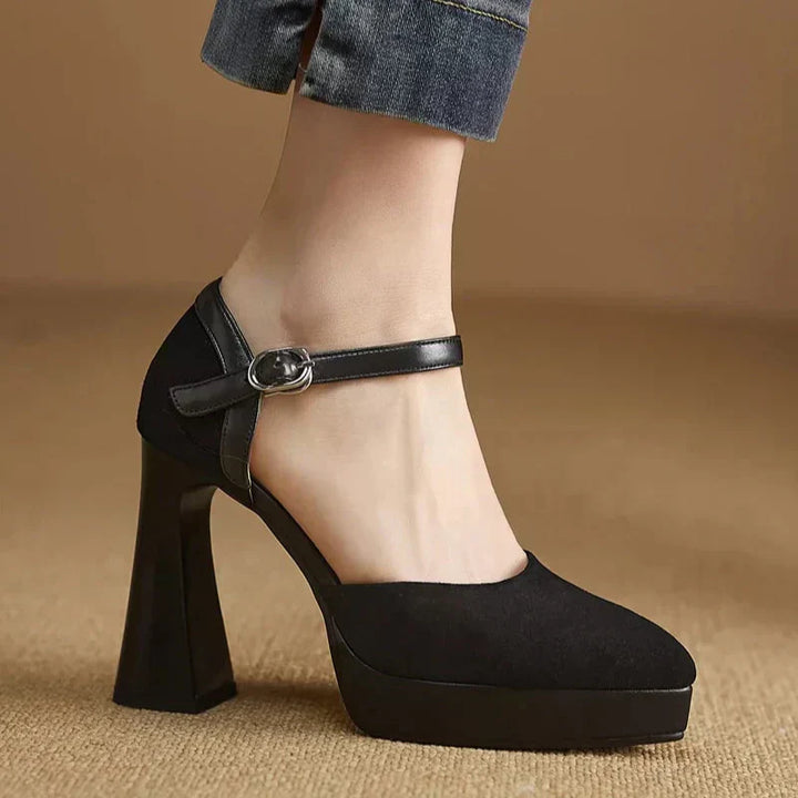 Female wearing stylish platform heel pumps with buckle ankle straps on a plain background.