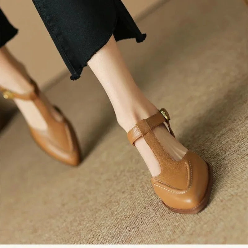 Woman wearing neutral t-strap buckle shoes on a plain background.